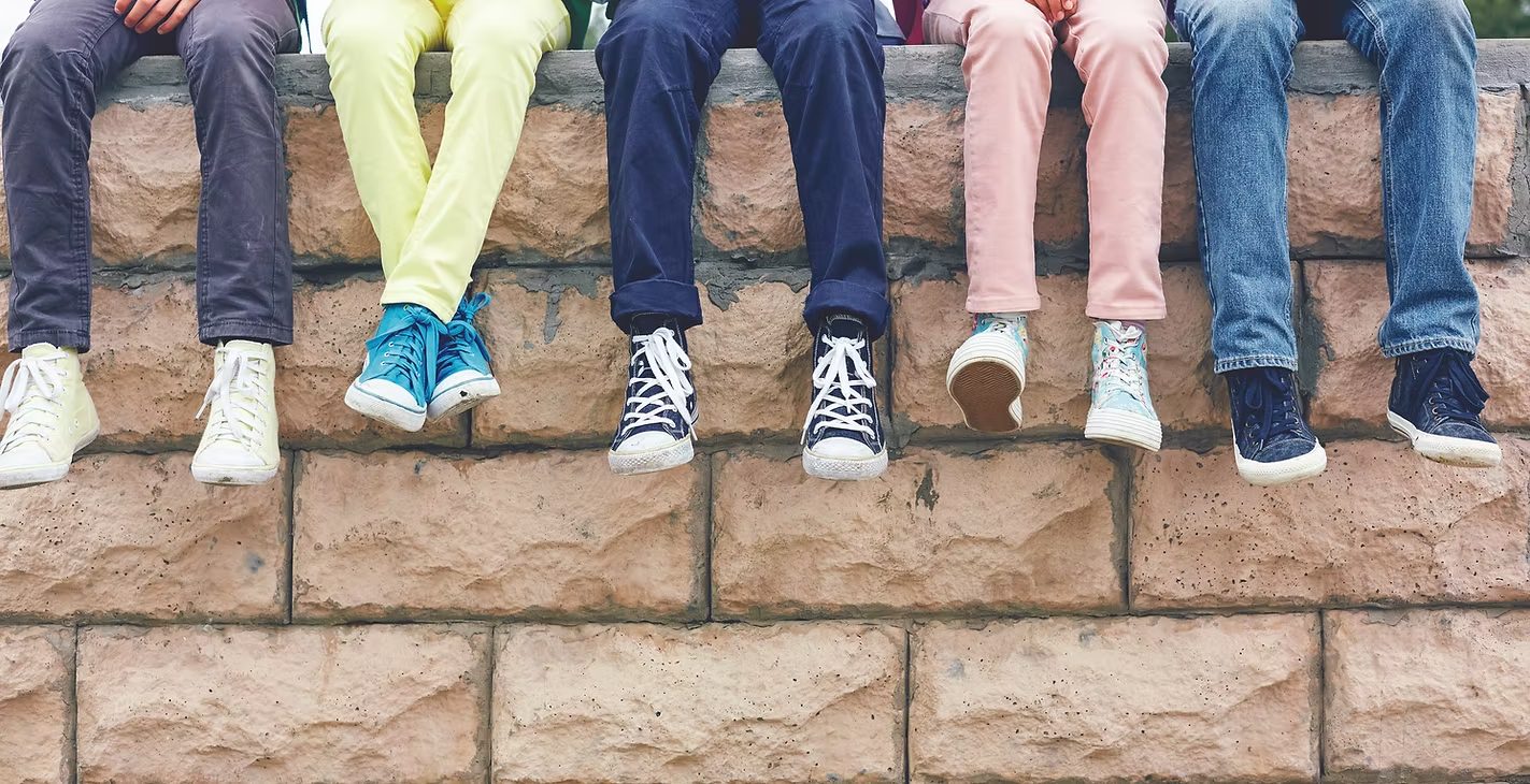 A row of children's sneakers and shoes lined up along a brick wall.
